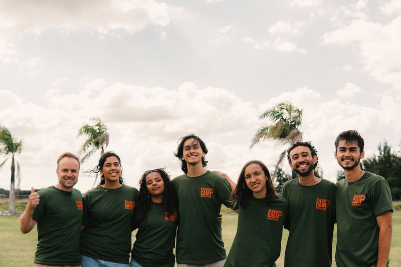 Seven counselors in green Swamp Camp Mexico shirts, arms around each other