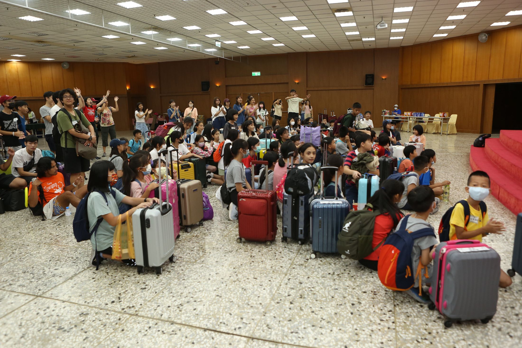 A hall full of campers sitting among rows of suitcases