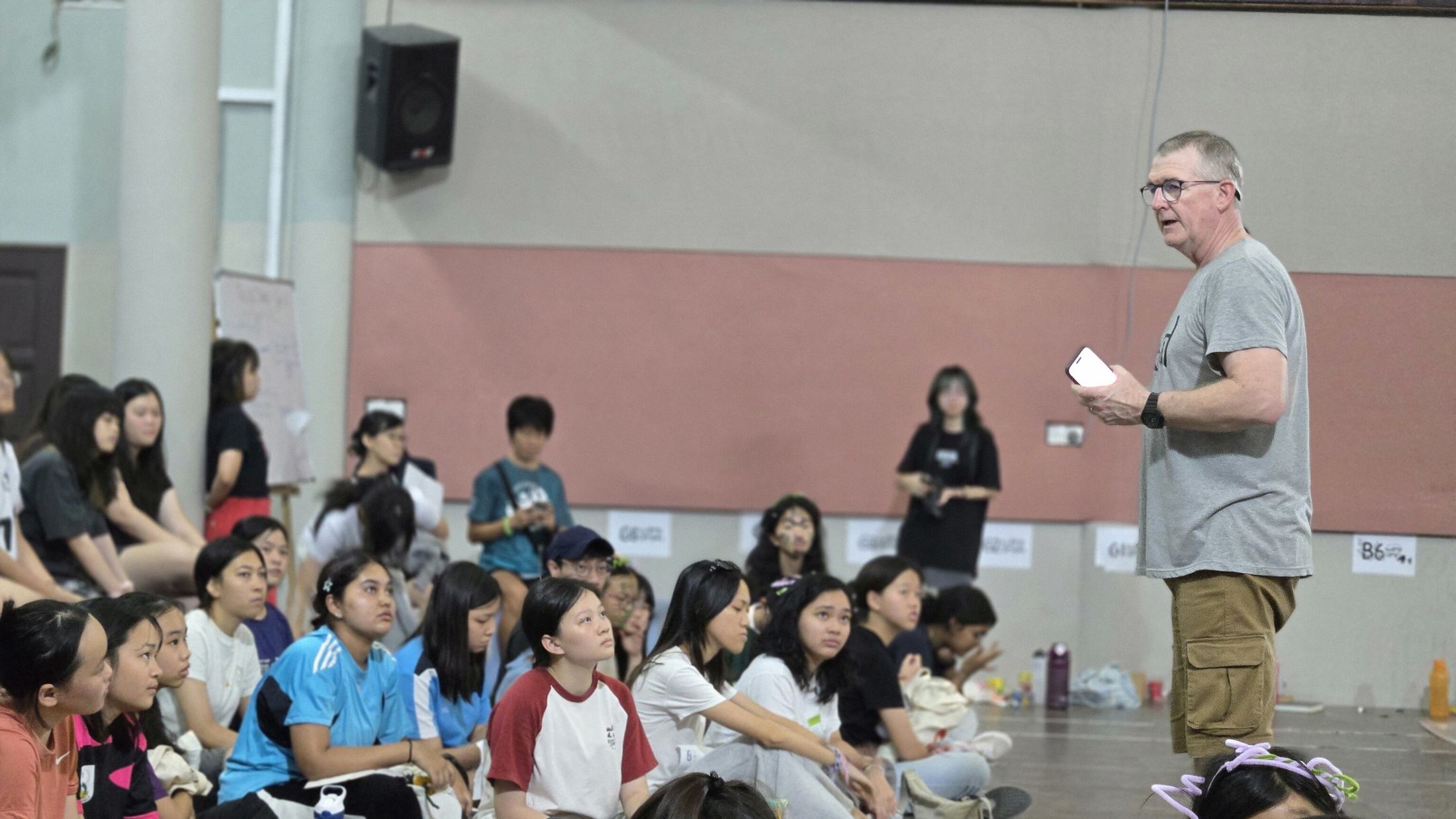 A leader speaking to campers seated on the hall floor