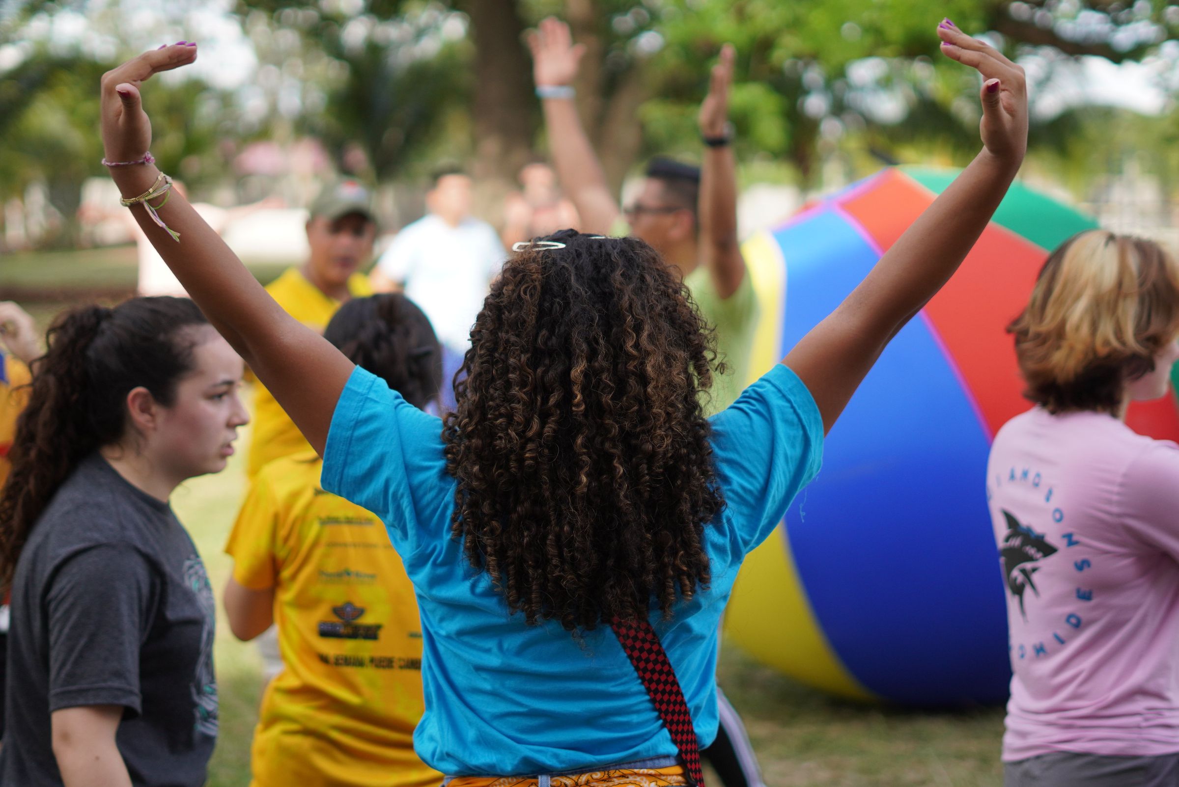 A counselor throws both arms in the air beside a giant rainbow earth ball at Swamp Camp Bolivia
