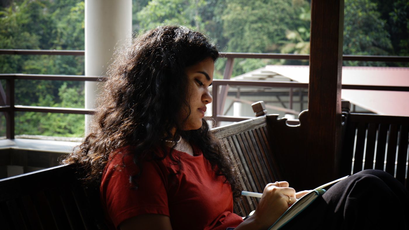 A young woman writing in a journal on a veranda above the jungle