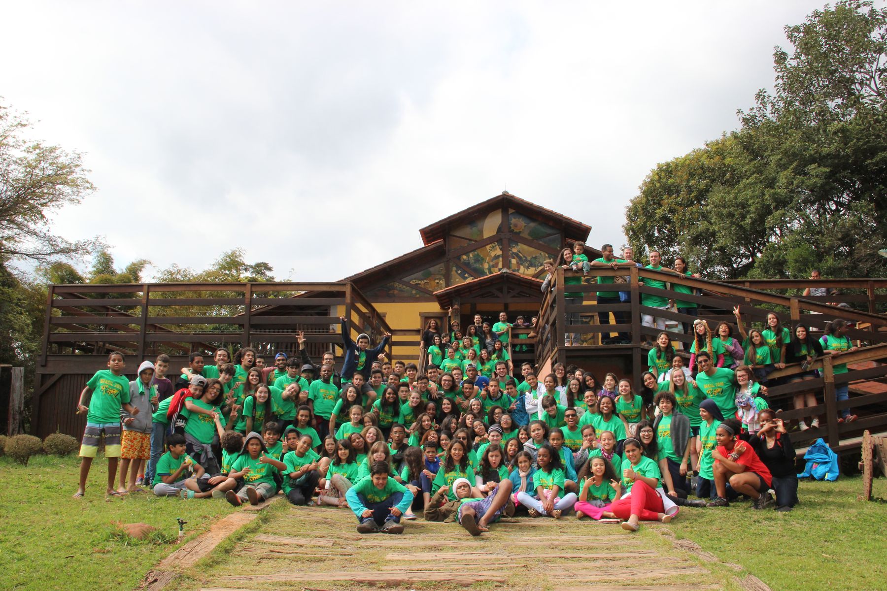 A camp in green shirts in front of a wooden lodge in Brazil