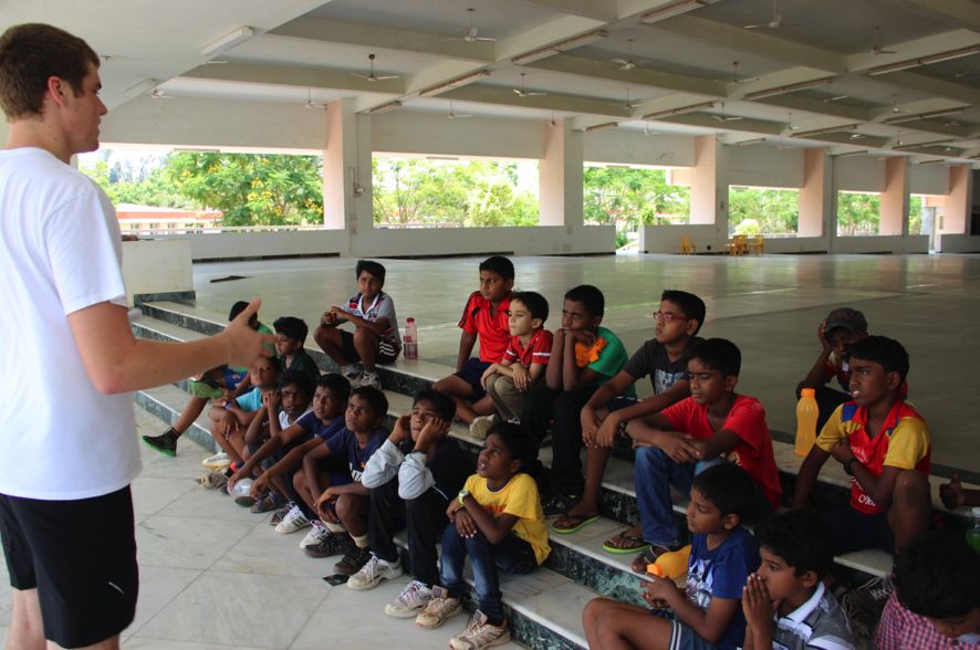A teacher leading a class of boys seated on wide steps under a pavilion