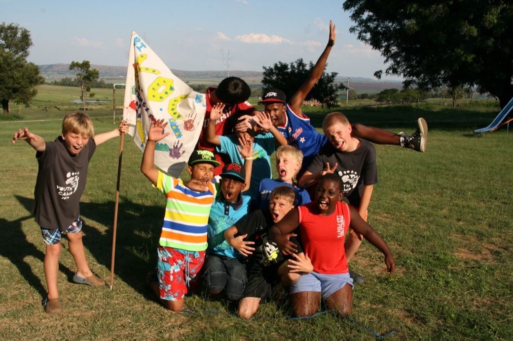 A team of boys piled together around their team flag on the camp lawn