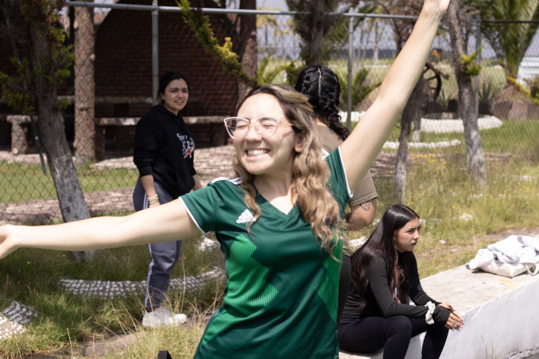 A counselor in a green Mexico jersey throwing her arms wide and laughing